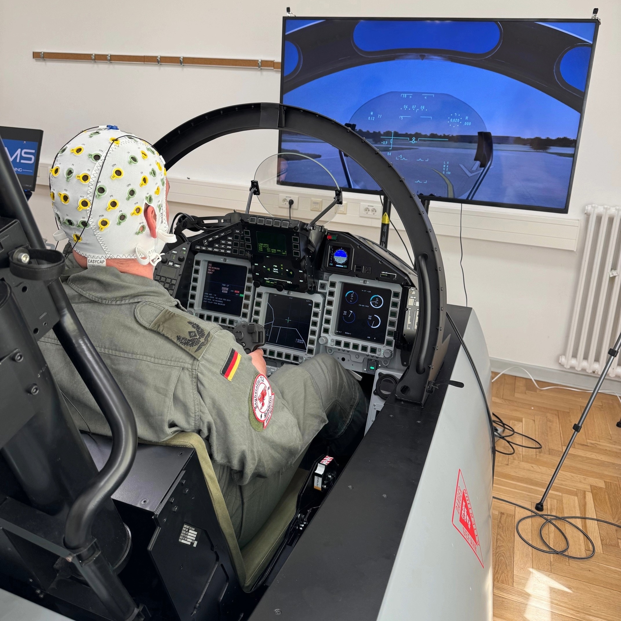 This Image shows the Cockpit only condition. A jet pilot inside the simulator seat, infront of a screen, showing the frontview of the virtual cockpit.