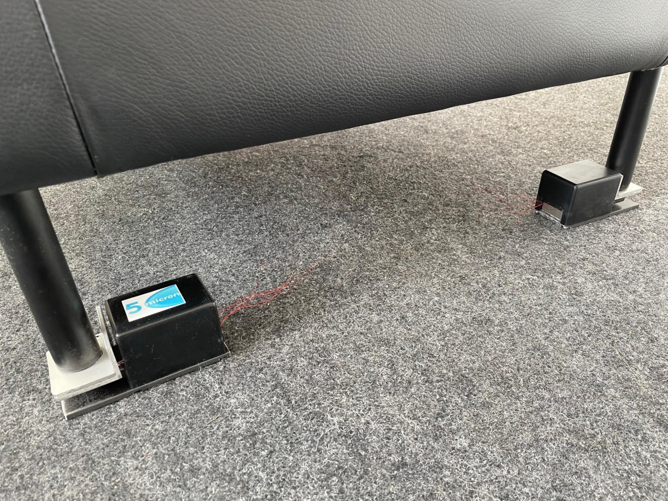 Two black sensor housings mounted on metal plates under the feet of a bed, connected by thin wires — the weight sensors the system measures with, out of the sleeper's way.